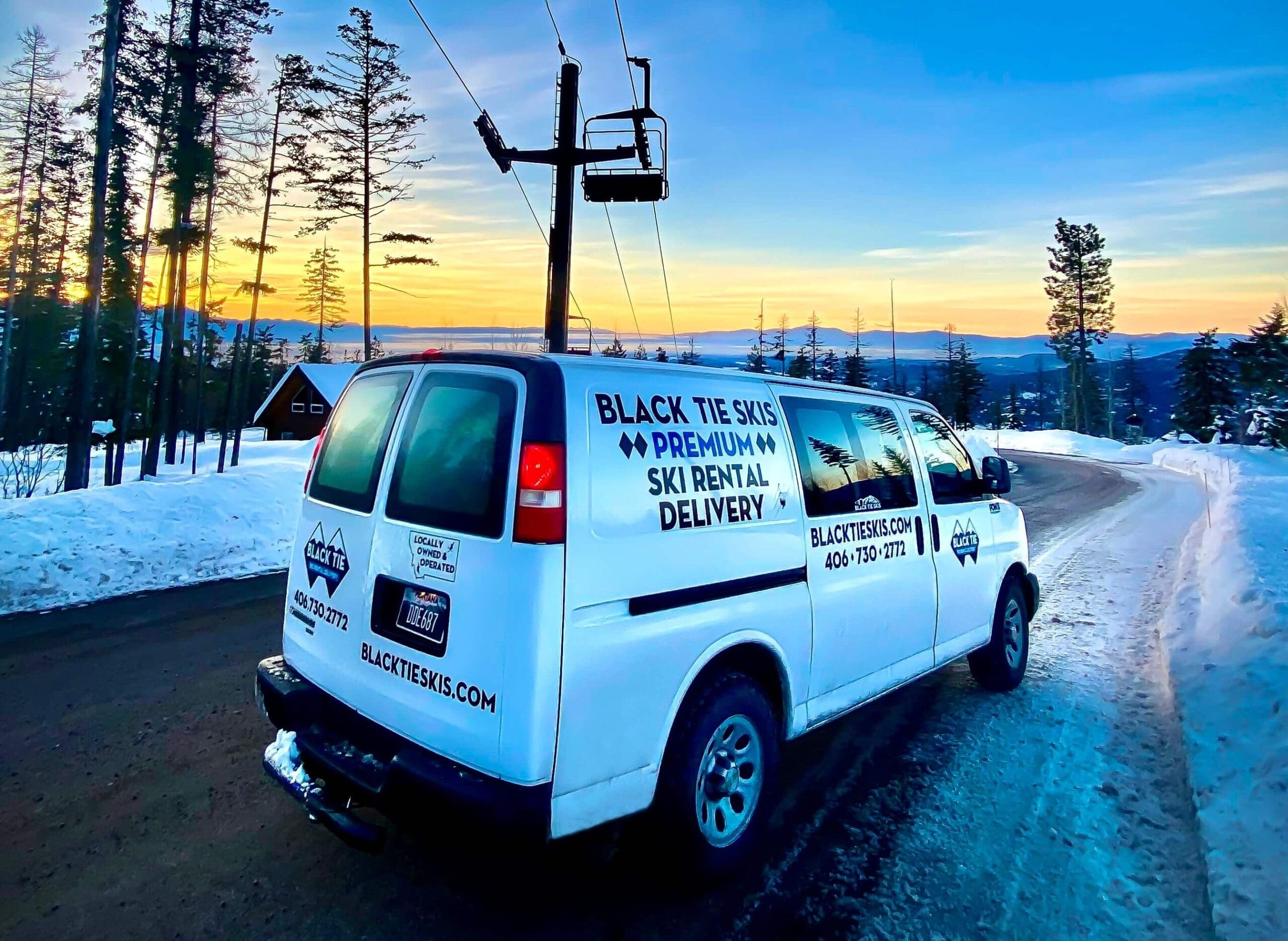 Black Tie Skis rental delivery van parked on a snowy mountain road at sunset