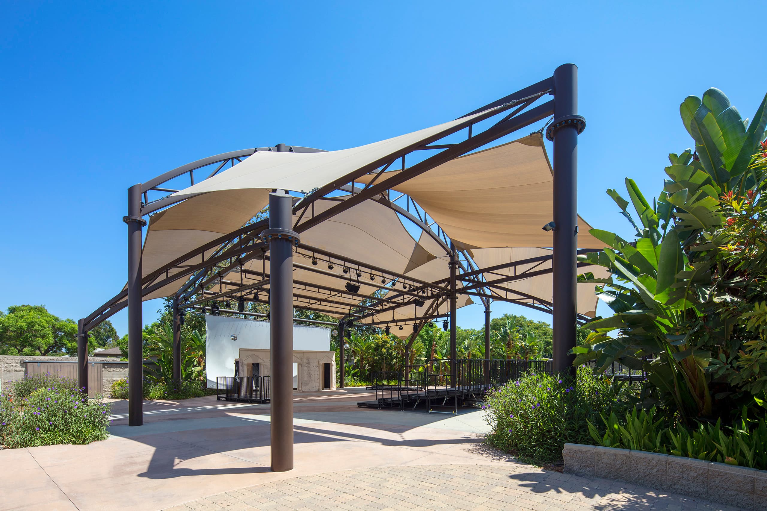Tensioned fabric shade sails covering an outdoor amphitheater stage and seating