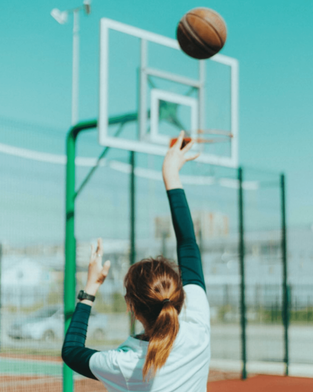 Person in athletic wear shooting a basketball toward an outdoor hoop